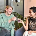 a couple of women sitting on top of a blue chair; bottleless water cooler office